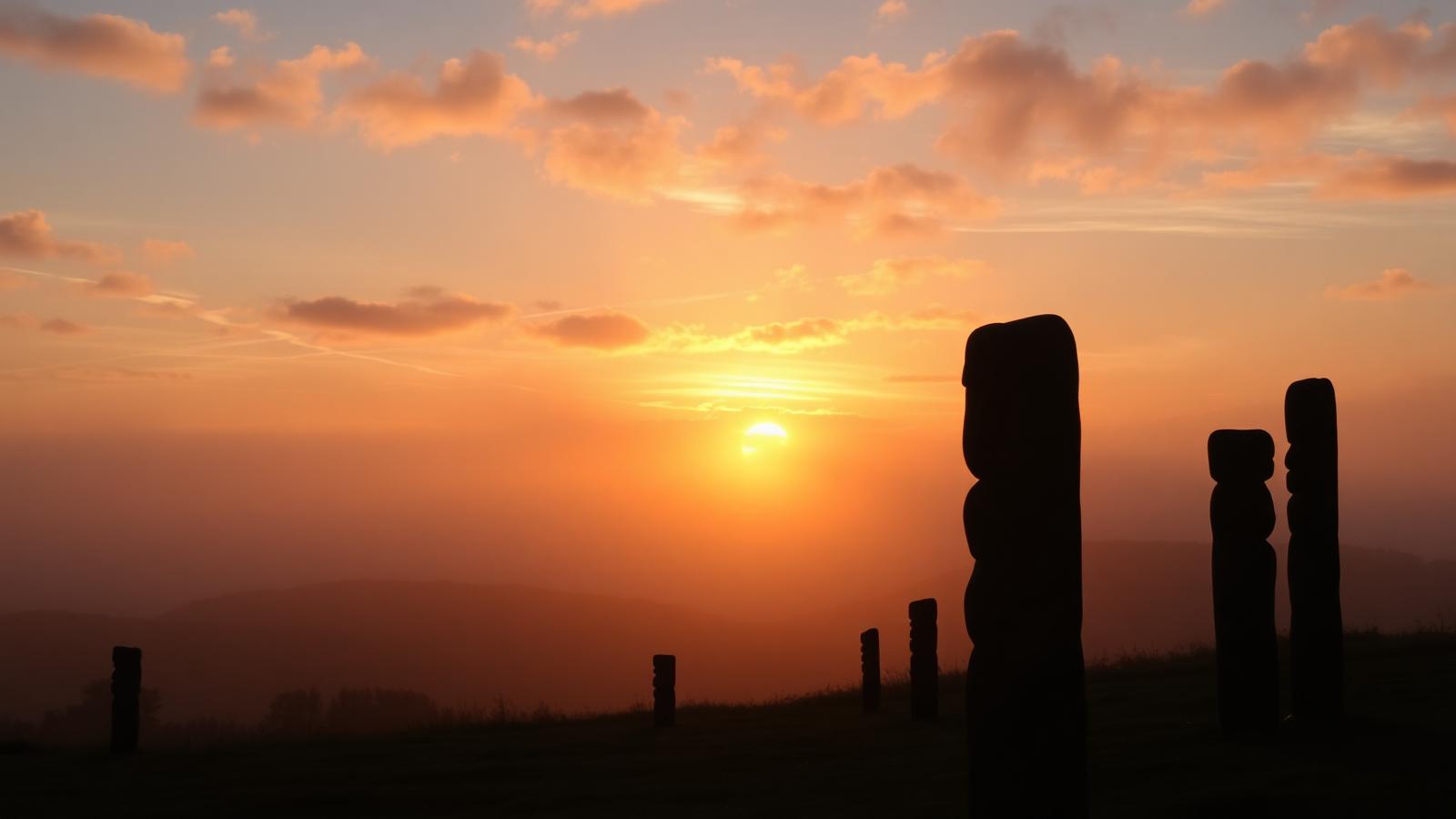 Sunrise over Aotearoa with carved pou whenua silhouetted against warm sky